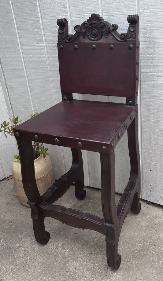 Dark wooden chair with decorative backrest against a white wall.